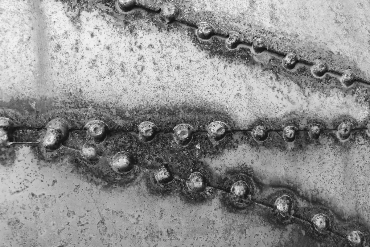 Raised weld beads running across an oxidised steel plate, close-up photograph in black and white
