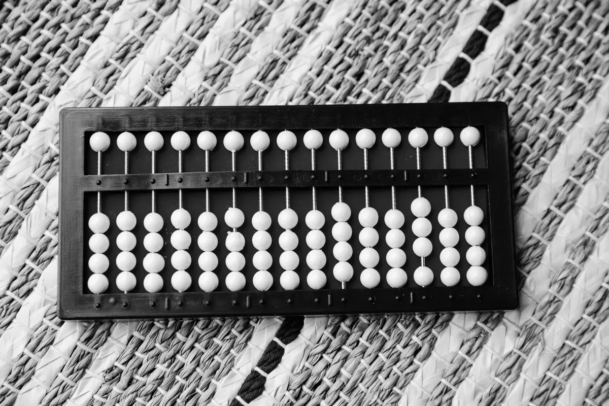 An abacus with rows of white beads on a red background, some rows more filled than others, close-up black and white photograph