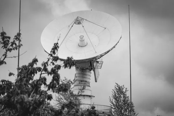 Grande antenna parabolica di una stazione di terra puntata verso un cielo nuvoloso, con parafulmini ai lati, fotografia in bianco e nero