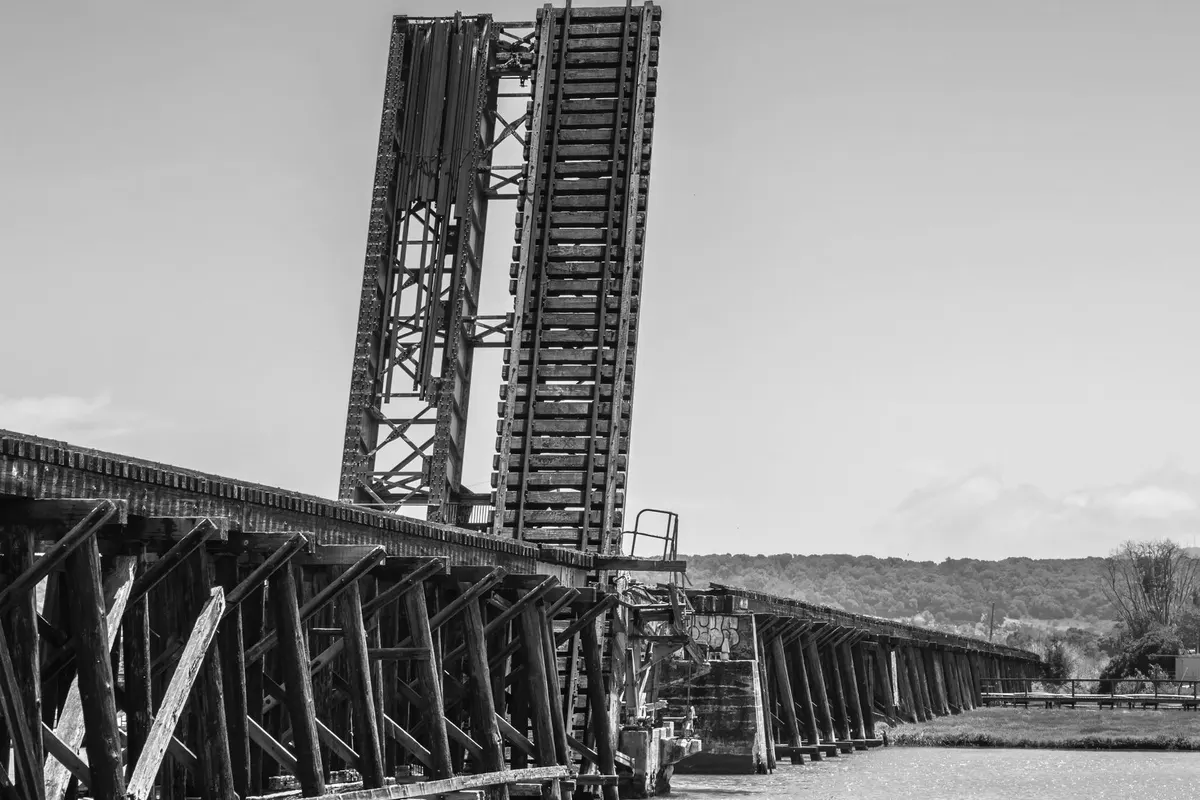 An old railway bascule bridge with its span raised above a river, timber and steel trusses, black and white photograph