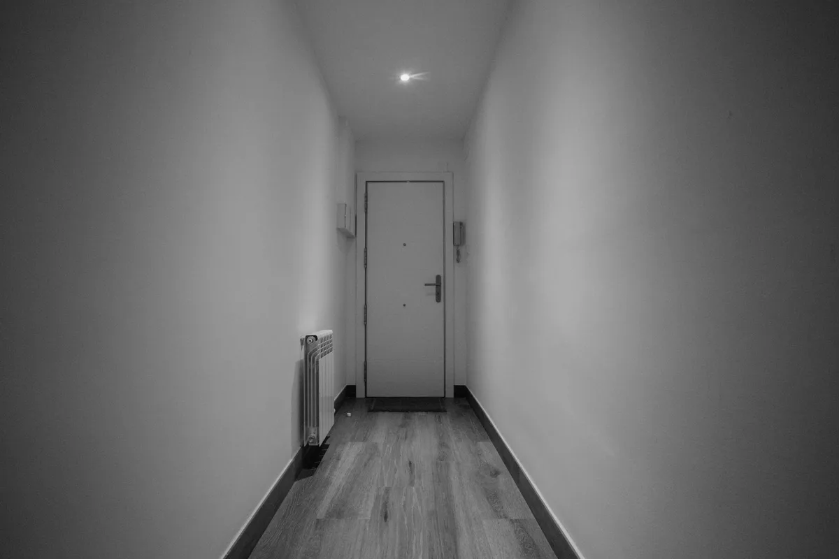Closed door at the end of a narrow, bare corridor, black-and-white photograph