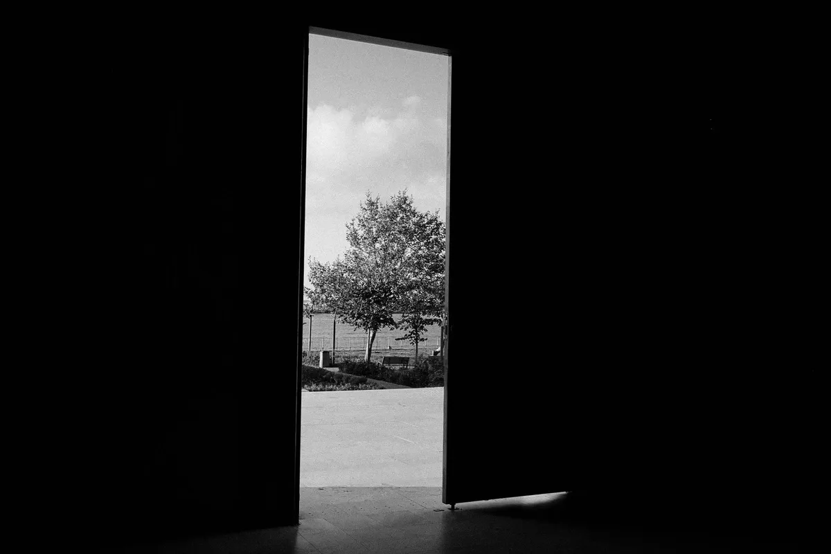 Threshold of an open interior door onto a bright exterior, black-and-white photograph, no people or writing