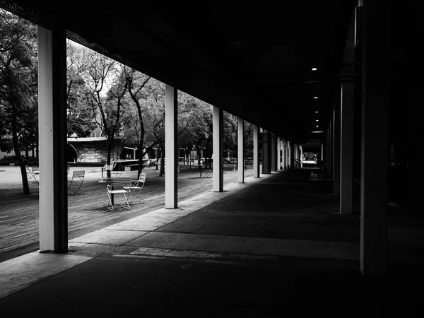 Portico deserto con file di sedie vuote sullo sfondo e prospettiva che fugge verso il buio, fotografia in bianco e nero