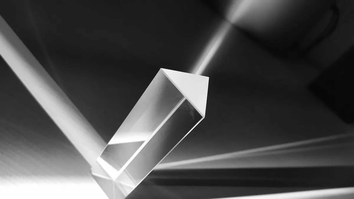 Prisma di vetro triangolare colpito da un fascio di luce che ne esce scomposto in una banda continua, in bianco e nero