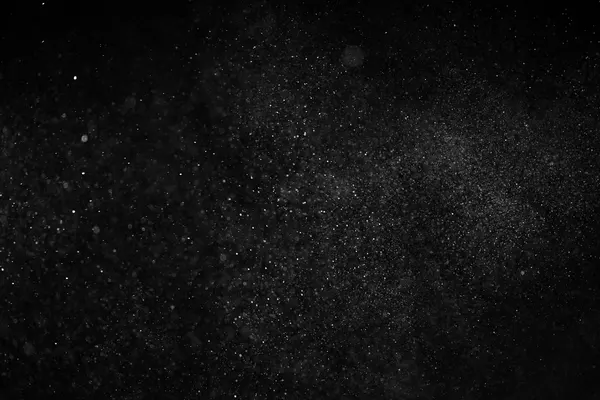 Pulviscolo sospeso in controluce su fondo scuro, particelle chiare di dimensioni diverse, nessuna persona