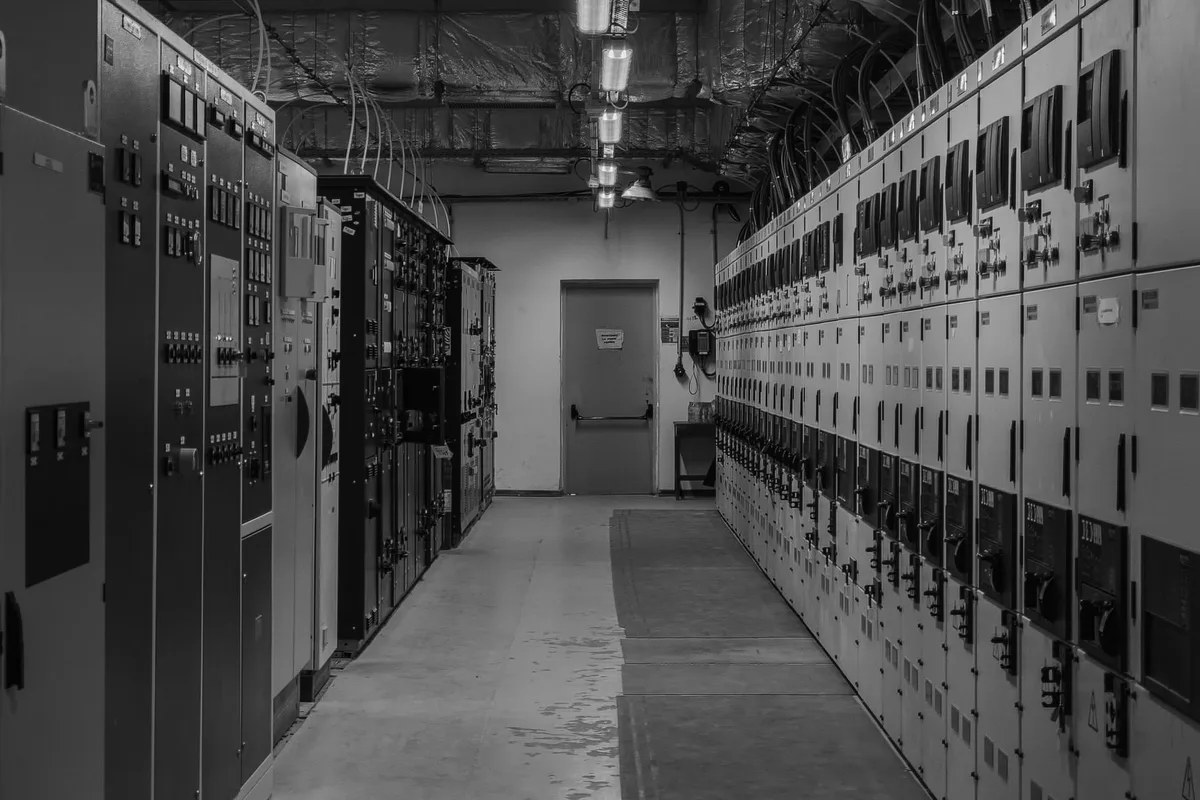 Corridor of an electrical distribution room with two rows of switchgear panels and measuring instruments, in black and white