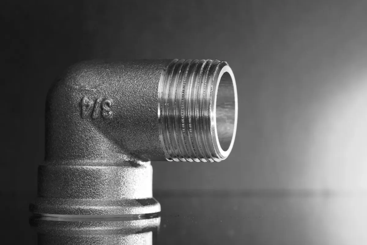 Brass elbow fitting with the size 3/4 cast in relief on its body, black and white photograph