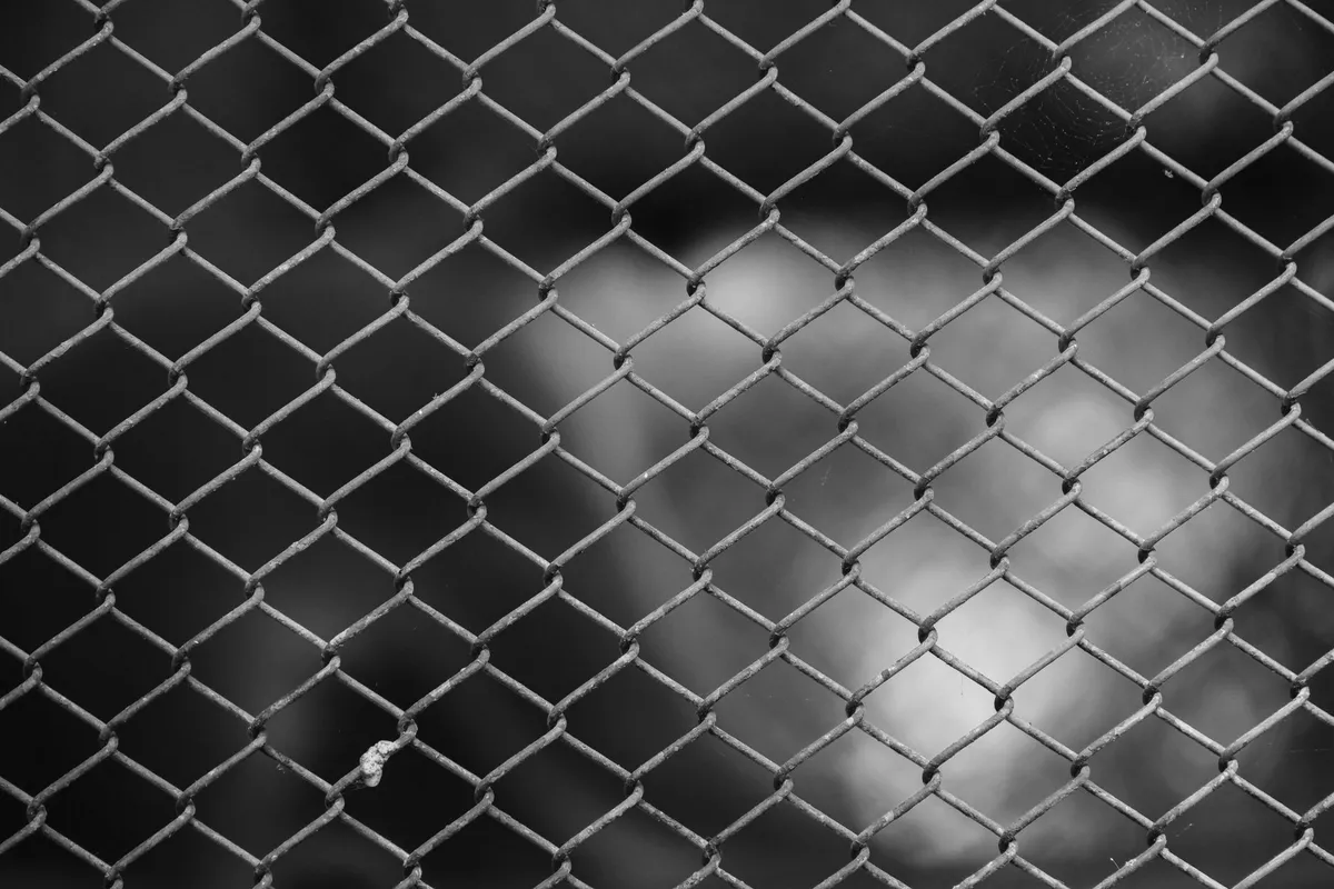 A black-and-white close-up of chain-link fencing, photographed up close with a blurred background