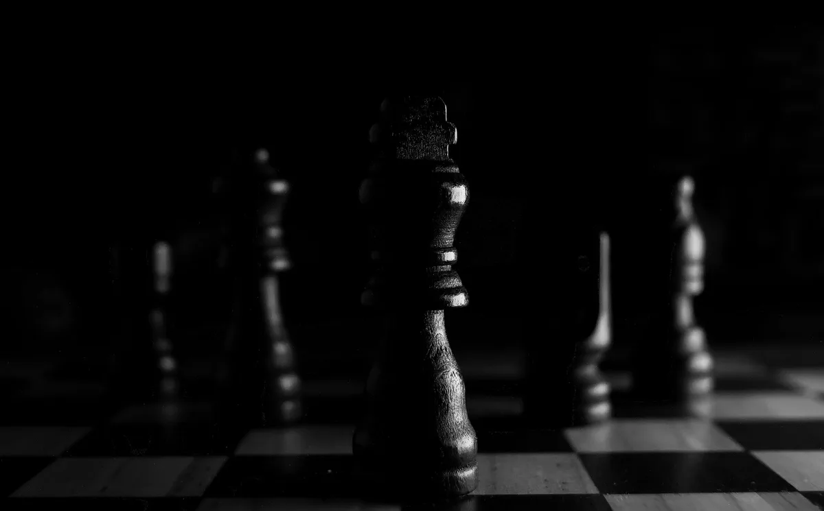 Close-up of a chess piece on a chessboard, other pieces blurred in the background, black-and-white photograph