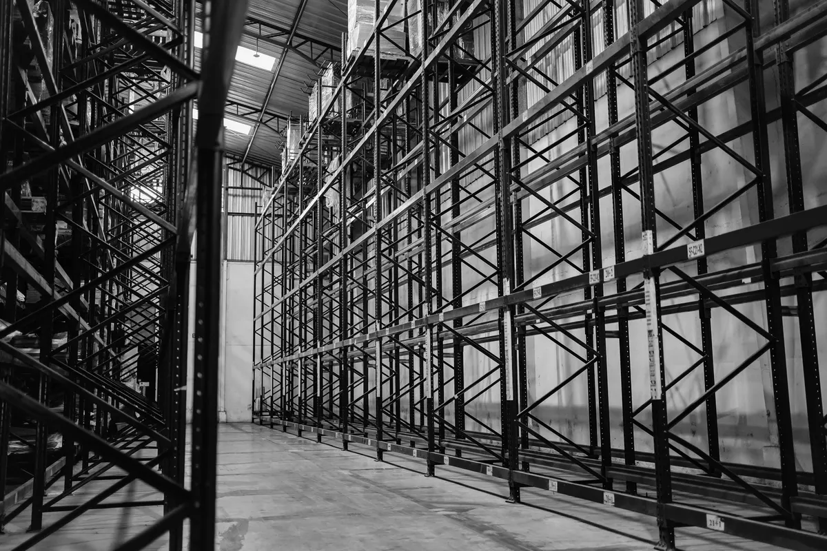 Corridoio di una scaffalatura industriale in acciaio, alta e completamente vuota, in un capannone logistico, fotografia in bianco e nero