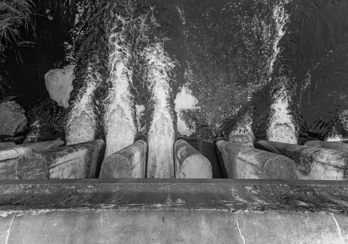 Concrete spillway channels seen from above, jets of water entering a basin, black-and-white photograph