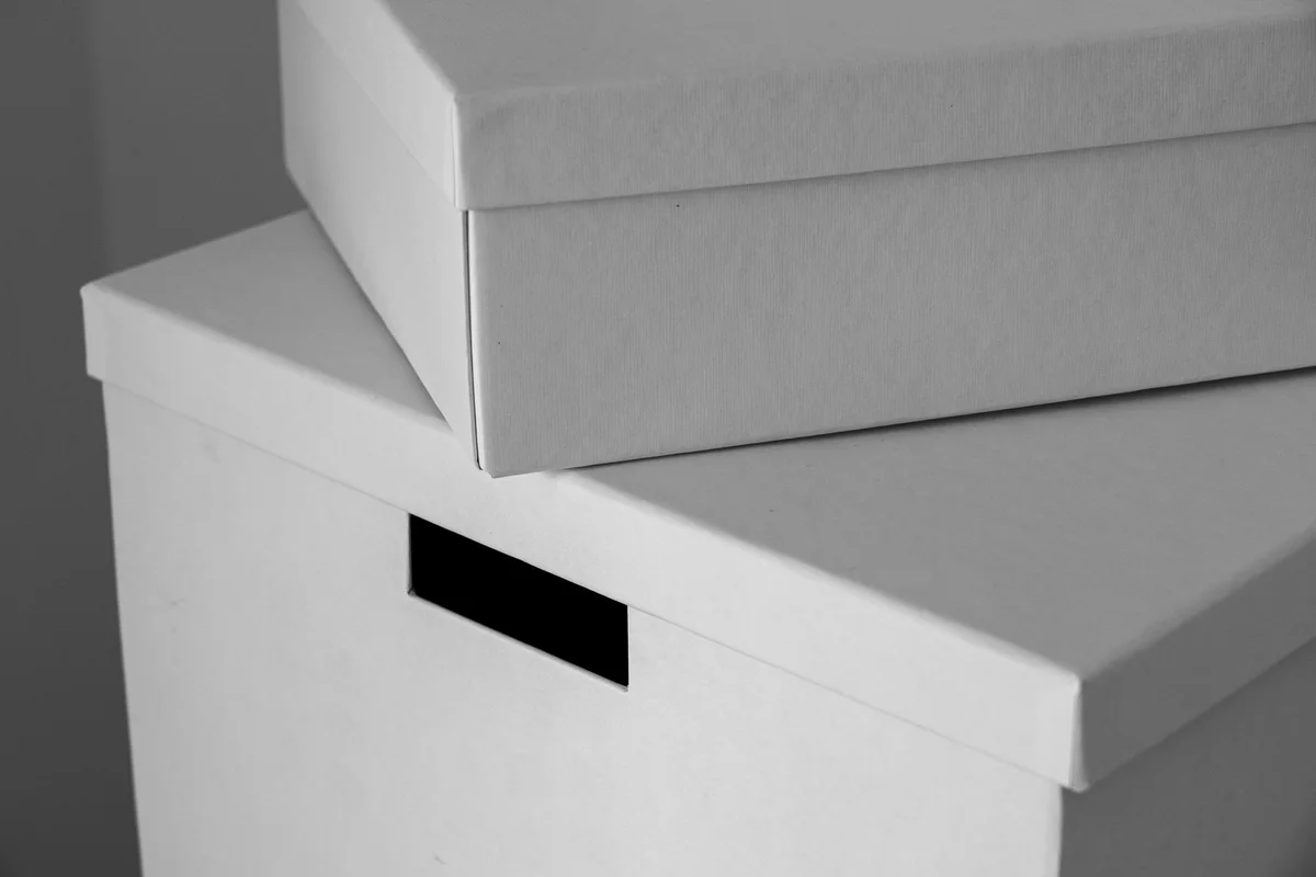 Identical plain white cardboard boxes stacked, black-and-white photograph