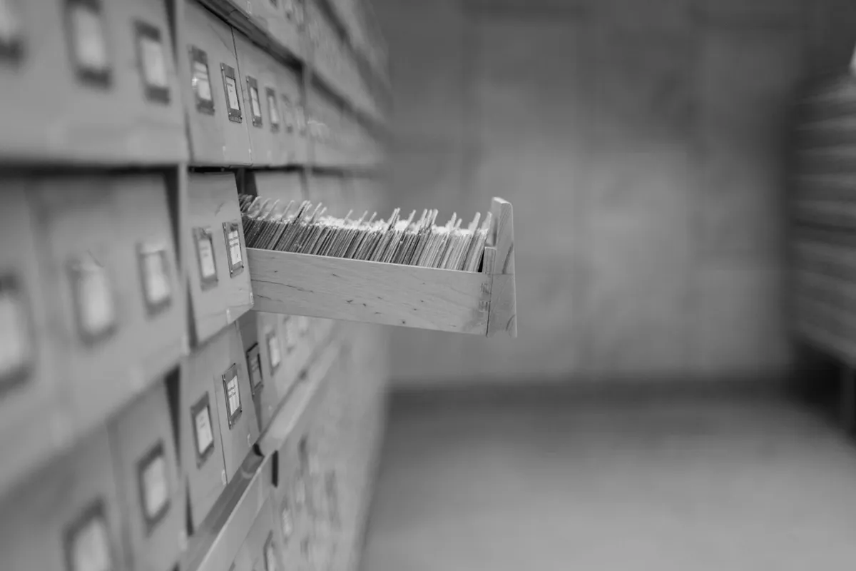 Wooden card-catalogue drawer pulled out among many others, filled with index cards, black-and-white photograph with no people or legible writing