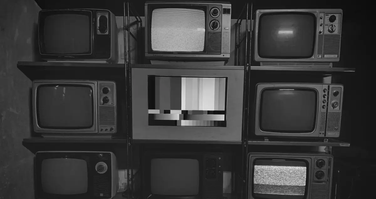 Parete di vecchi televisori impilati su scaffali, uno mostra il disturbo e uno una barra di calibrazione, fotografia in bianco e nero