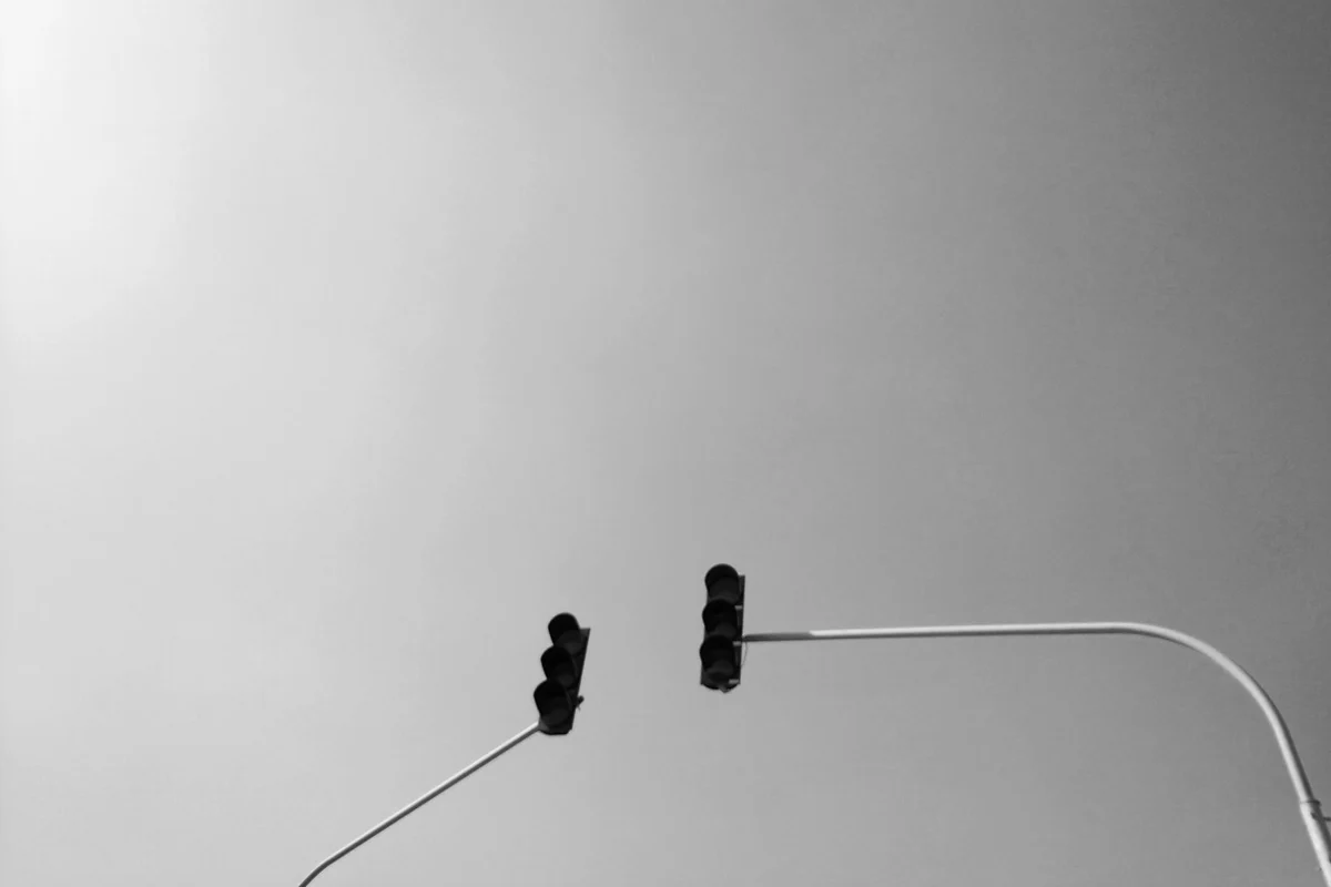 Due lanterne semaforiche spente su bracci curvi contro un cielo coperto, fotografia in bianco e nero, nessuna persona