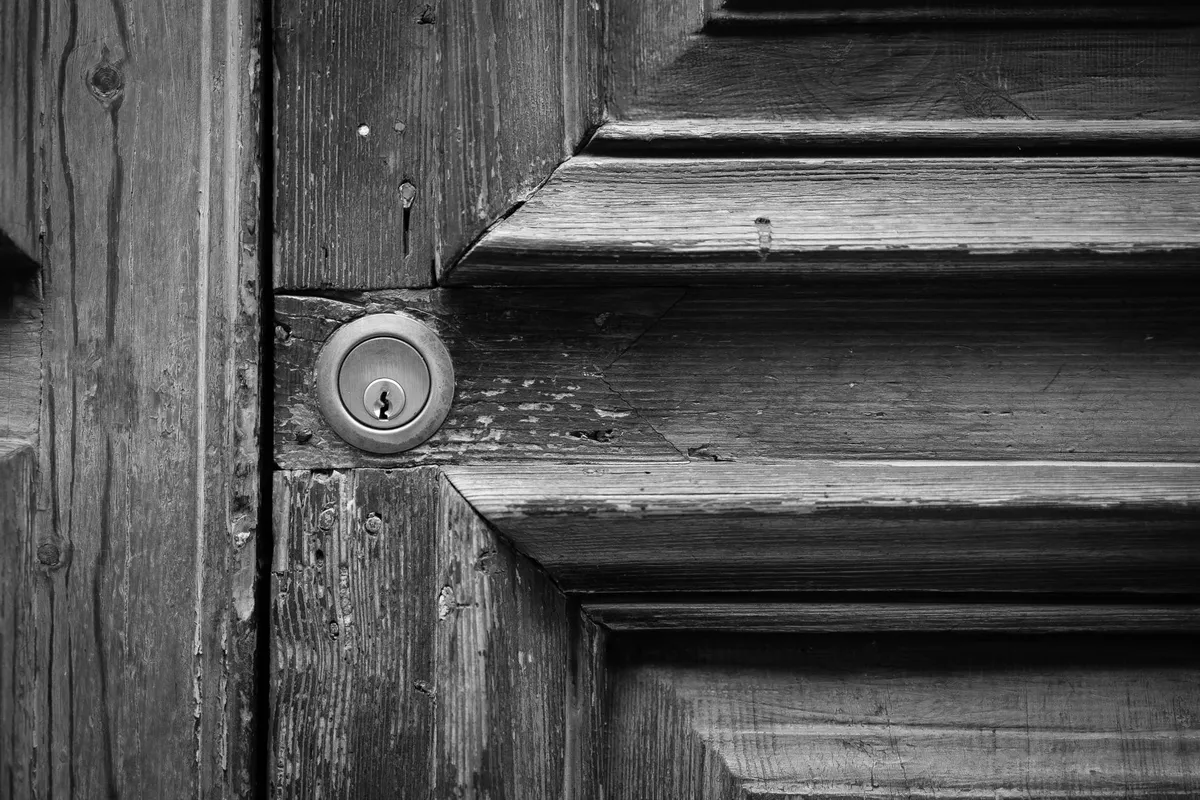 Vecchia serratura in ottone su una porta di legno scuro, con la cornice del pannello visibile intorno, in bianco e nero