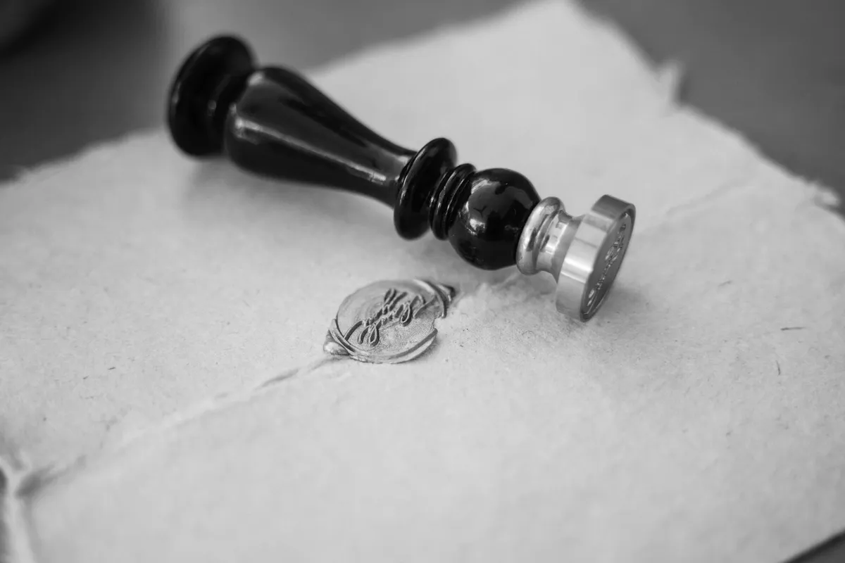 A dark metal wax-seal stamp resting on light paper, next to the impression it has left, in black and white