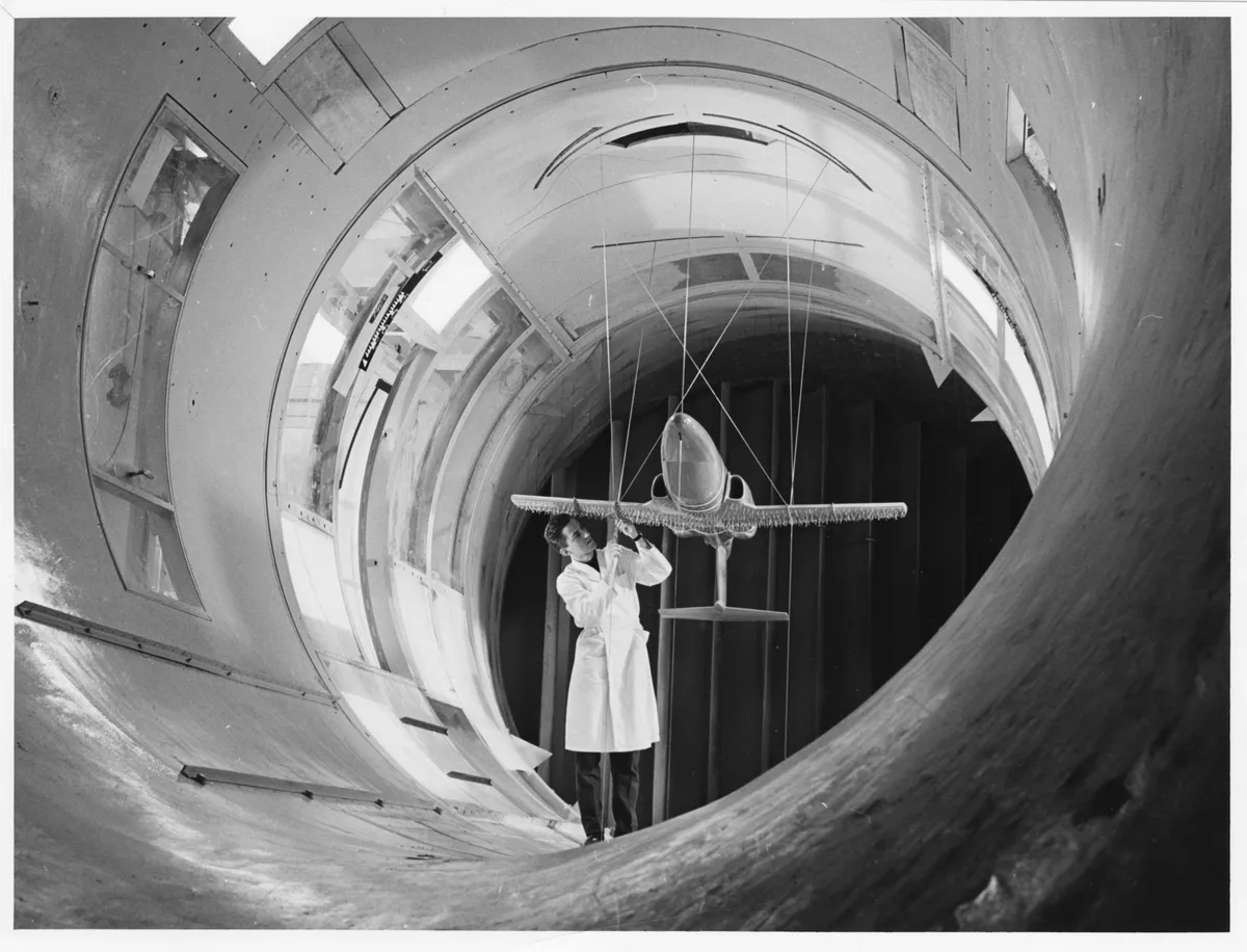 A technician testing a model aircraft in a wind tunnel