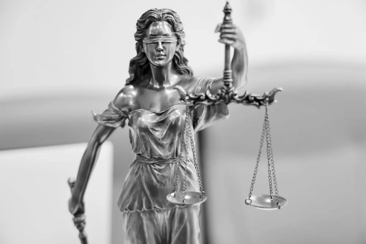 Statuetta metallica della Giustizia bendata, con bilancia e spada, fotografata da vicino in bianco e nero