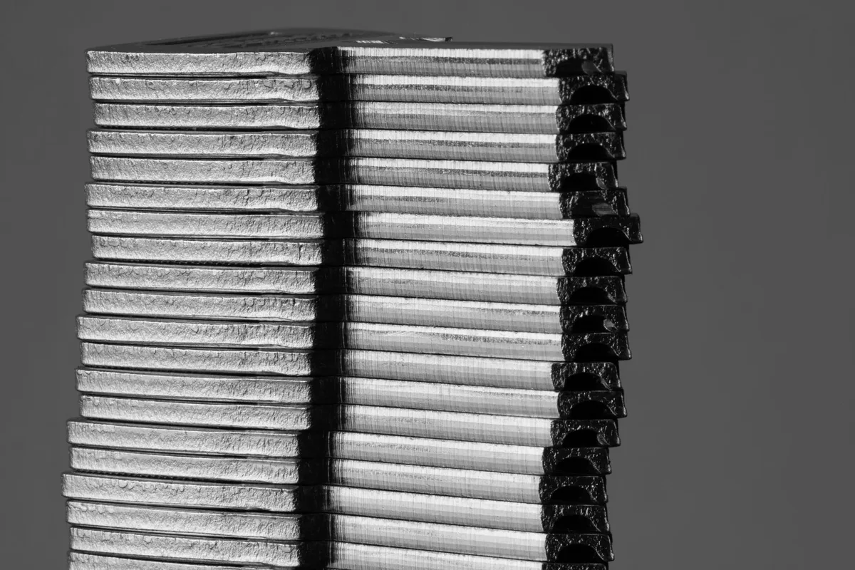Close-up of a stack of thin metal plates piled one on top of another against a plain grey background