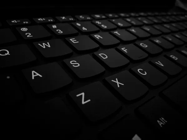 Primo piano in bianco e nero dei tasti di una tastiera per computer, ripresi lateralmente in controluce