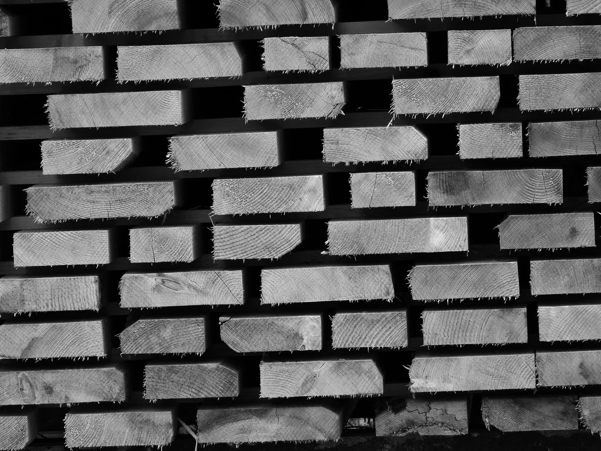 Cut ends of sawn wooden planks stacked on spacers, photographed close up in black and white