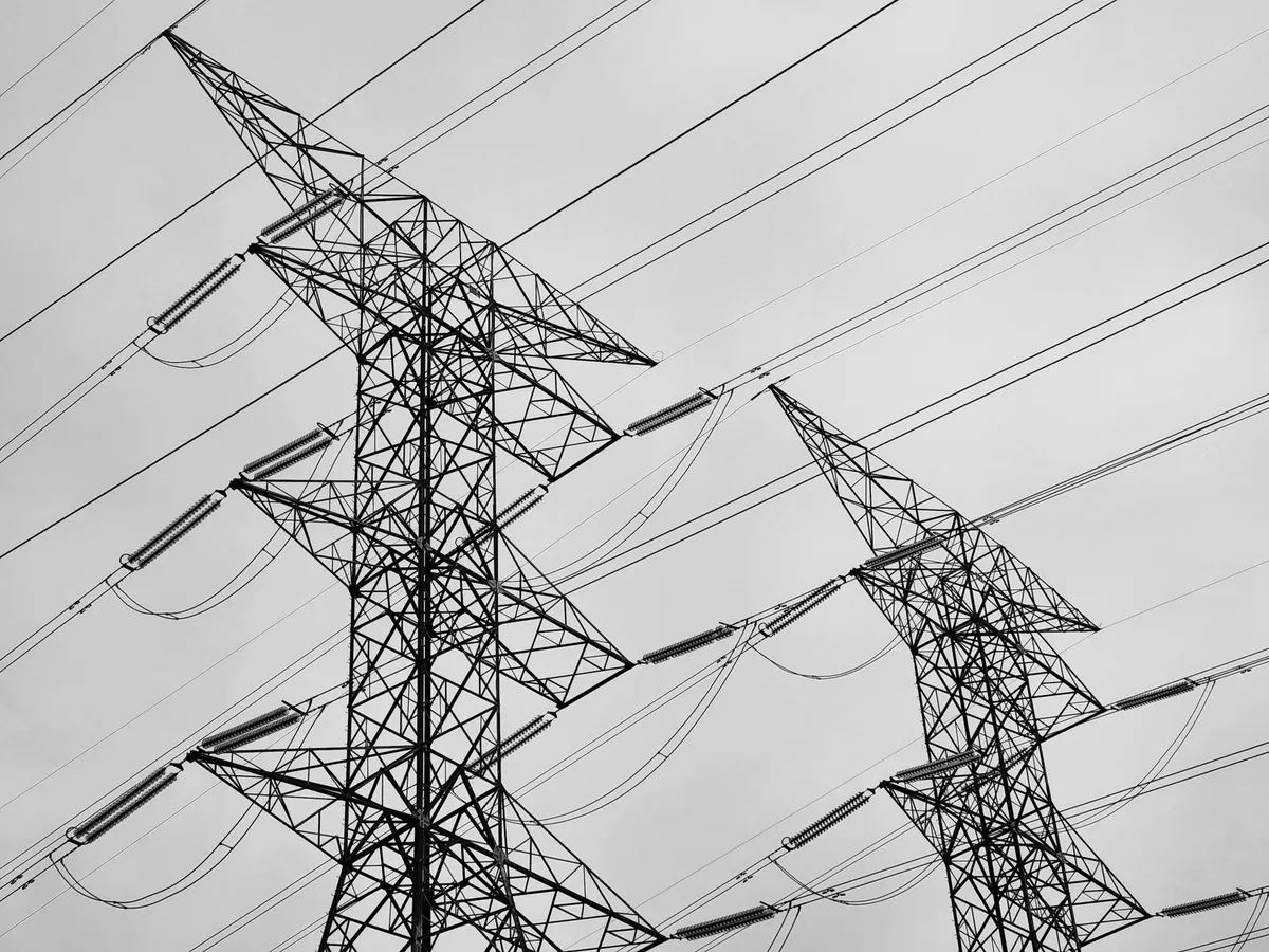 Black-and-white high-voltage transmission towers, taut power lines against a flat sky