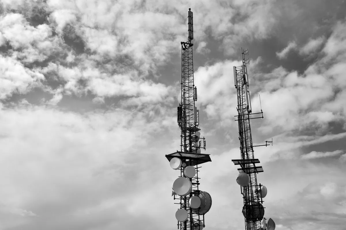 Two transmission masts with antennas and dishes against a cloudy sky, black-and-white photograph