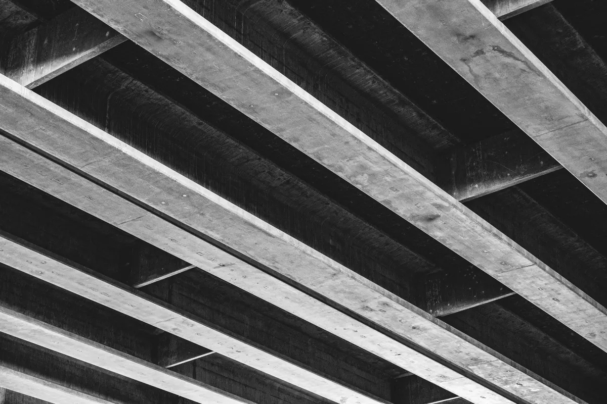 Travi in cemento riprese dal basso, che si incrociano in diagonale a formare un reticolo regolare, fotografia in bianco e nero, nessuna persona